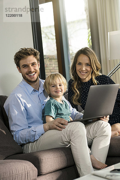 Porträt der glücklichen Eltern und des Sohnes auf dem Sofa mit Laptop zu Hause