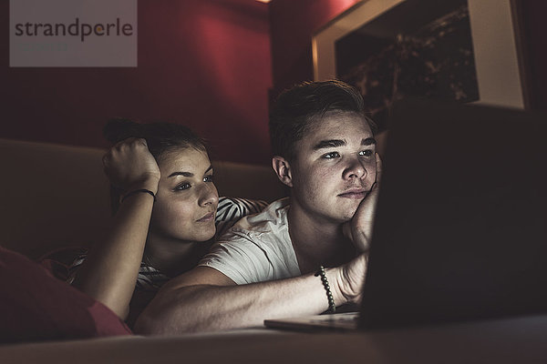 Paar im Bett liegend zu Hause mit Blick auf den Laptop