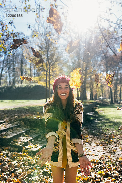 Porträt einer schönen  fröhlichen Frau  die sich mit Blättern in einem herbstlichen Wald amüsiert.