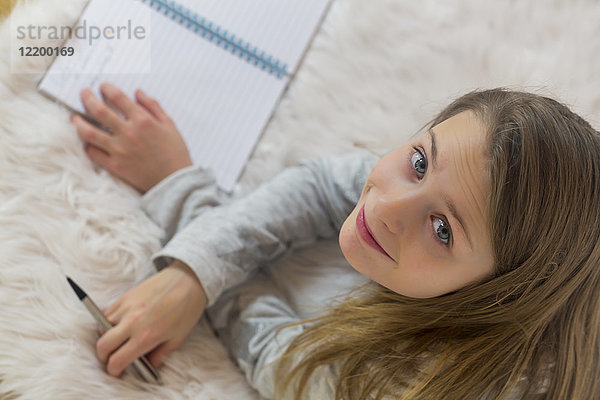 Porträt eines lächelnden Mädchens  das mit Bleistift und Broschüre auf dem Boden liegt.