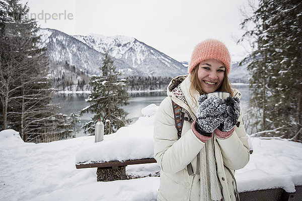 Porträt einer lächelnden jungen Frau in alpiner Winterlandschaft mit See