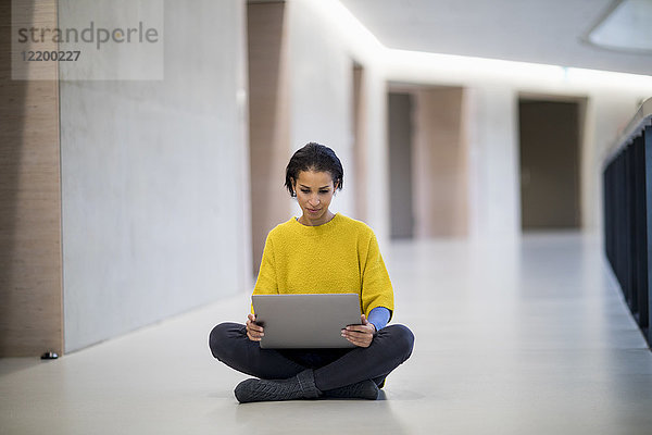 Porträt einer jungen Frau mit gelbem Pullover auf dem Boden sitzend mit Laptop