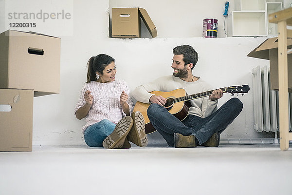 Ein Paar sitzt auf dem Boden und spielt Gitarre.
