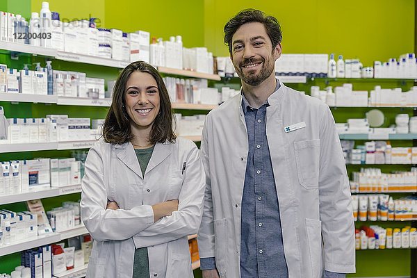 Porträt zweier lächelnder Apotheker im Regal mit Medikamenten in der Apotheke
