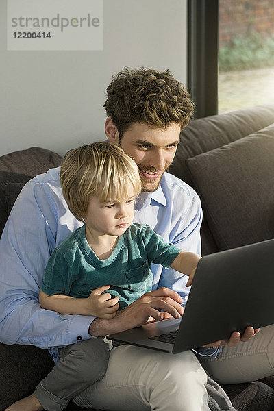 Vater und Sohn betrachten Laptop auf der Couch zu Hause