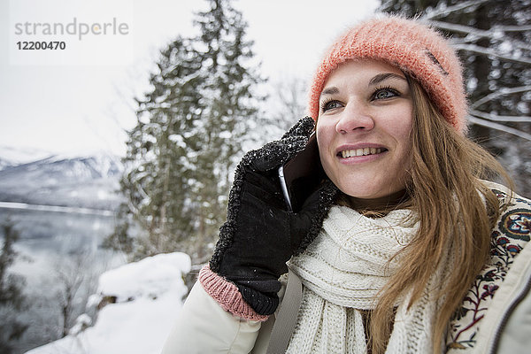 Porträt einer lächelnden jungen Frau am Handy in alpiner Winterlandschaft