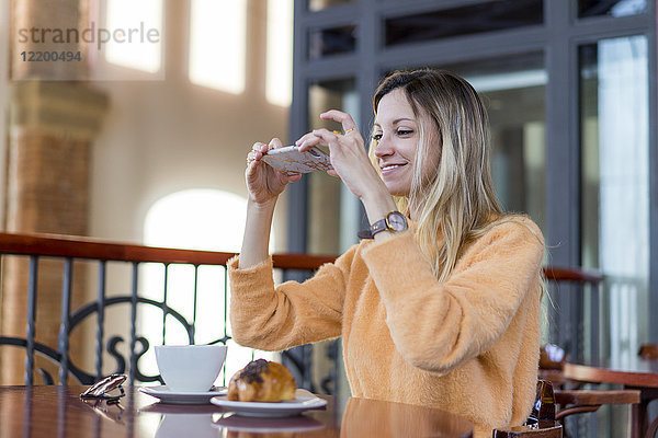 Lächelnde junge Frau in einem Café beim Fotografieren von Handys