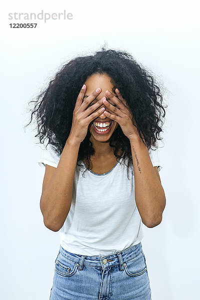 Porträt einer lachenden jungen Frau  die die Augen mit den Händen bedeckt.