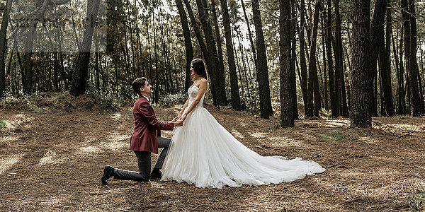 Mann kniend macht Heiratsantrag an glückliche Braut im Wald