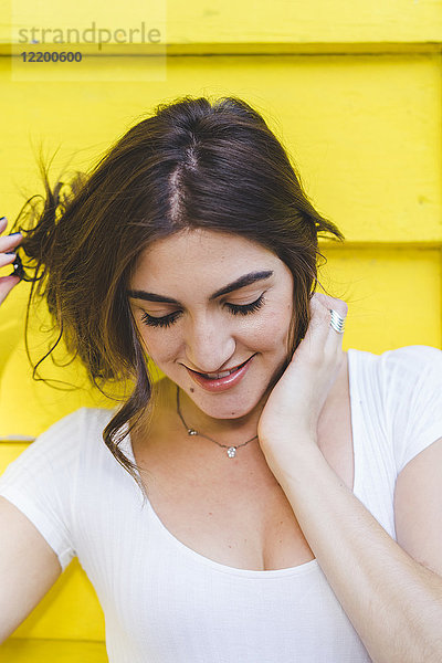 Porträt einer lächelnden jungen Frau vor gelber Holzwand mit Blick nach unten