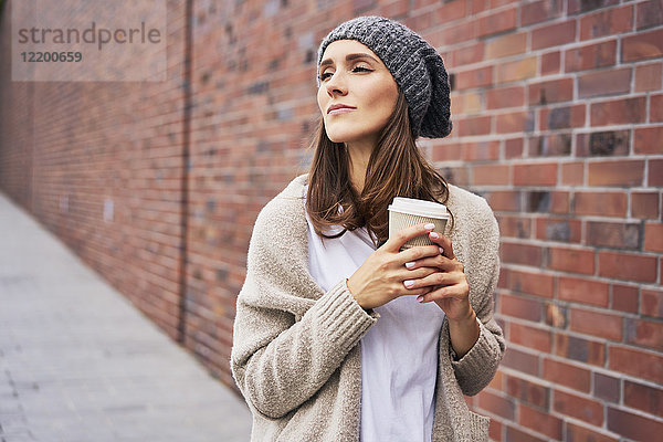 Porträt einer träumenden jungen Frau mit Kaffee zum Mitnehmen