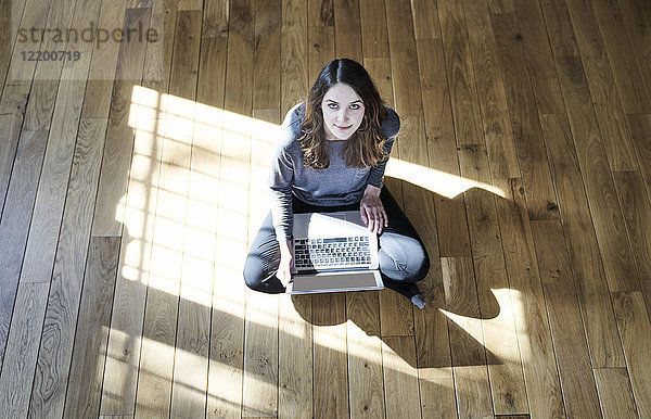 Portrait einer jungen Frau mit Laptop auf Holzboden