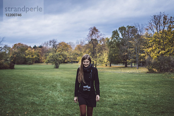 Junge Frau mit Kamera läuft auf einer Wiese im Herbstpark