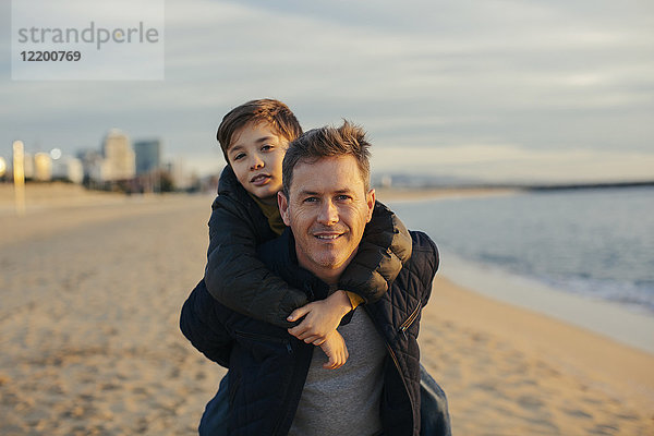 Porträt des Vaters  der seinen Sohn huckepack am Strand trägt.