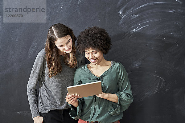 Zwei lächelnde junge Frauen teilen sich das Tablett vor der Tafel.