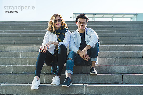 Porträt eines stilvollen jungen Paares  das auf einer Treppe im Freien sitzt