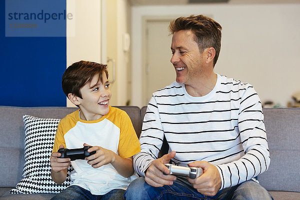 Glücklicher Vater und Sohn spielen Videospiel auf der Couch zu Hause