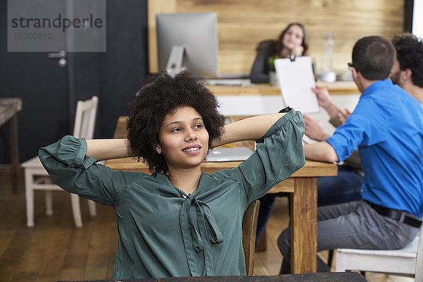 Junge Frau denkt im Büro mit Mitarbeitern im Hintergrund