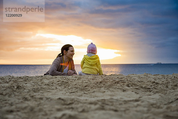 Mutter mit kleiner Tochter am Strand bei Sonnenuntergang