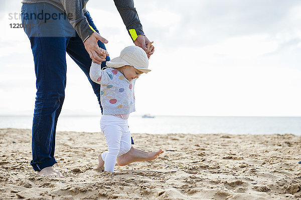 Spanien  Lanzarote  kleines Mädchen  das mit Hilfe seines Vaters am Strand spazieren geht.