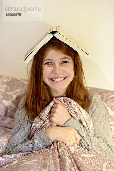 Porträt eines lachenden rothaarigen Teenagermädchens mit Buch auf dem Kopf