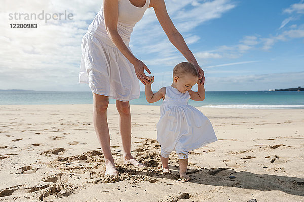 Mutter hilft der kleinen Tochter  die am Strand spazieren geht.