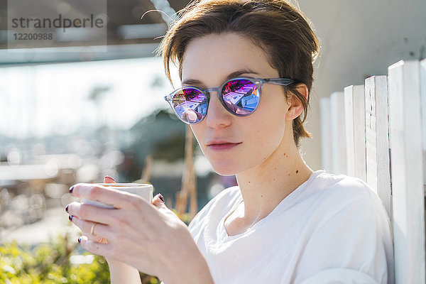 Porträt einer Frau mit Tasse Kaffee und verspiegelter Sonnenbrille