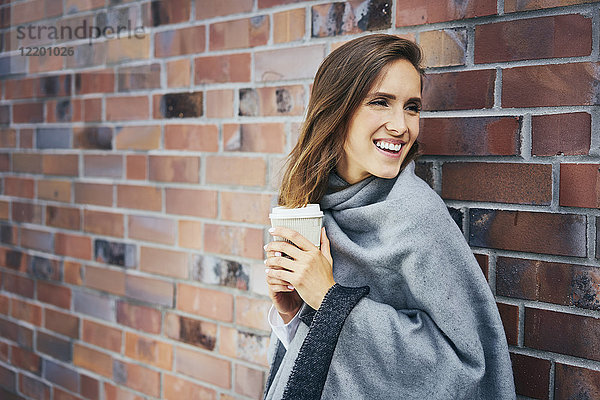 Porträt einer jungen Frau mit Kaffee vor der Backsteinmauer