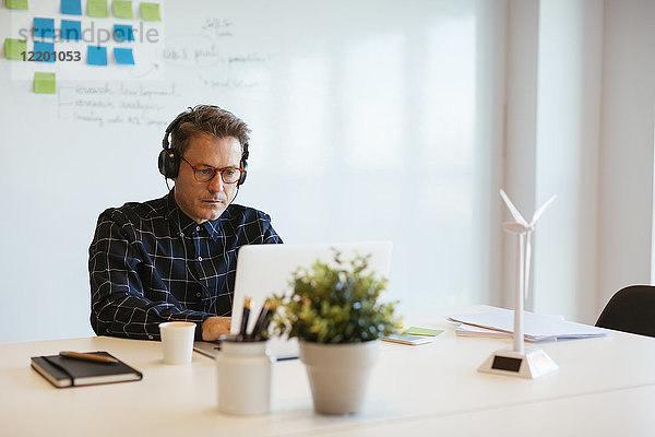 Geschäftsmann mit Kopfhörer über Laptop am Schreibtisch im Büro