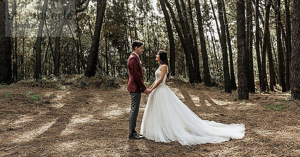 Braut und Bräutigam stehen im Wald und halten sich an den Händen.