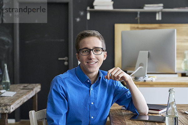 Porträt eines lächelnden jungen Mannes am Holztisch im Büro