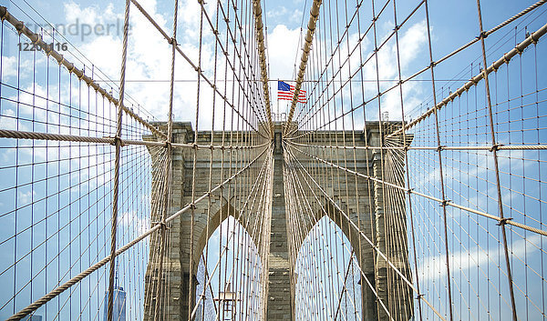 USA  New York  Brooklyn  Nahaufnahme von Brooklyn Bridge Metallkabeln und Bögen mit amerikanischer Flagge an der Spitze