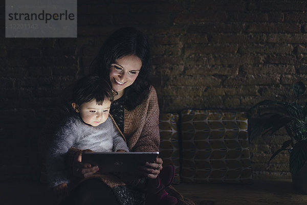 Mutter und Tochter mit digitalem Tablett zu Hause im Dunkeln