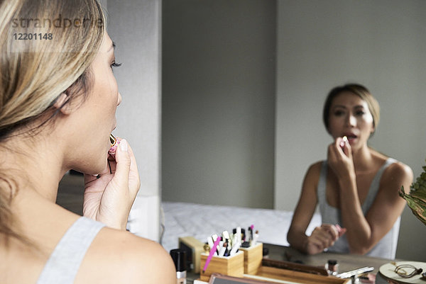 Frau zu Hause mit Make-up und Lippenstift vor dem Spiegel