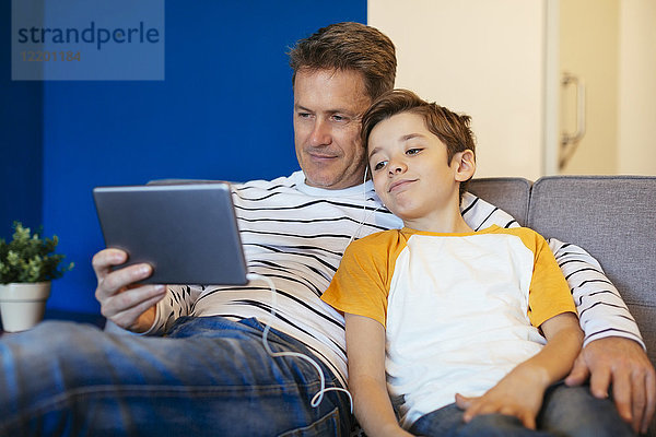 Vater und Sohn mit Ohrstöpseln und Tablette auf der Couch zu Hause