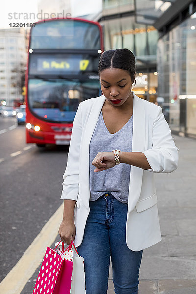 UK  London  Frau mit Einkaufstüten in der Stadt  die die Zeit überprüft.