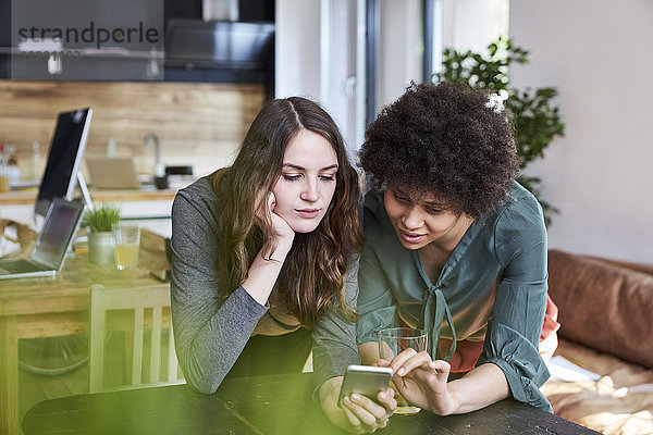 Zwei junge Frauen teilen sich ihr Handy im modernen Büro.