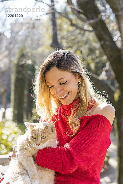 Glückliche junge Frau mit einer Katze im Garten