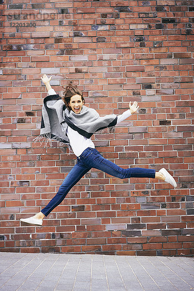 Fröhliche junge Frau  die vor der Ziegelmauer in die Luft springt.