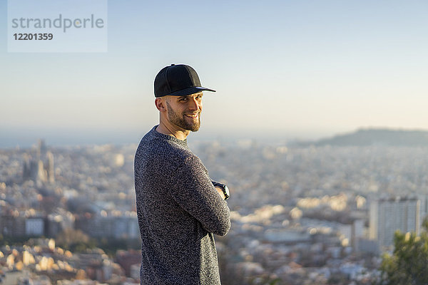Spanien  Barcelona  lächelnder junger Mann auf einem Hügel mit Blick auf die Stadt