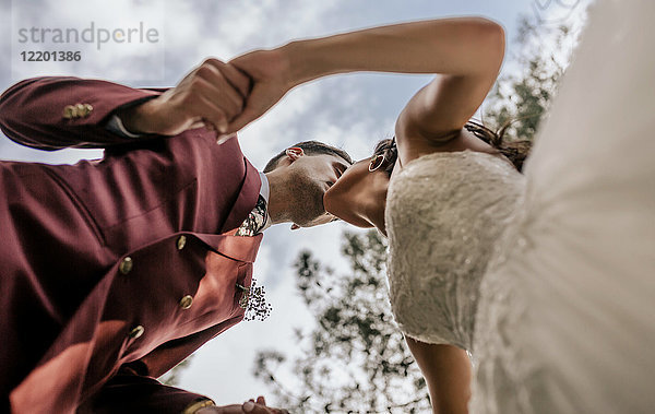 Braut und Bräutigam beim Händchenhalten und Küssen mit Himmel im Hintergrund