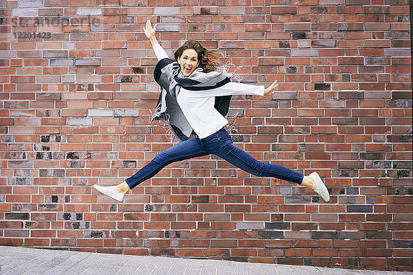 Fröhliche junge Frau  die vor der Ziegelmauer in die Luft springt.