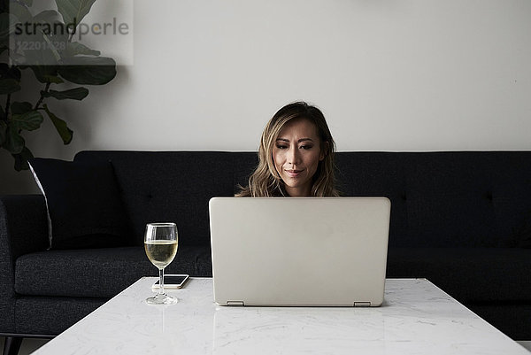 Frau zu Hause mit Laptop und Glas Wein