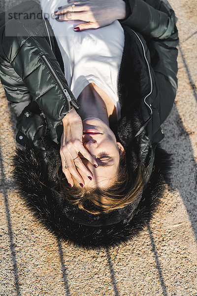 Porträt einer Frau mit Kapuzenjacke  die bei Sonnenlicht auf dem Boden liegt.