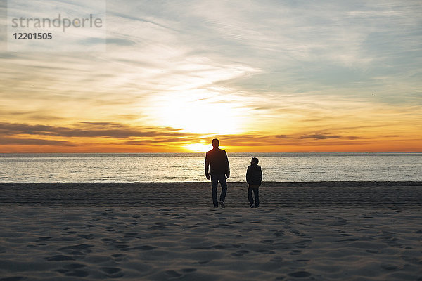 Vater und Sohn gehen bei Sonnenuntergang am Strand spazieren.
