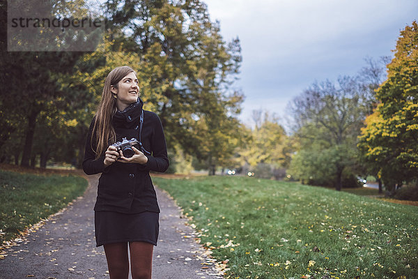 Junge Frau mit Kamera beim Spaziergang im Herbstpark