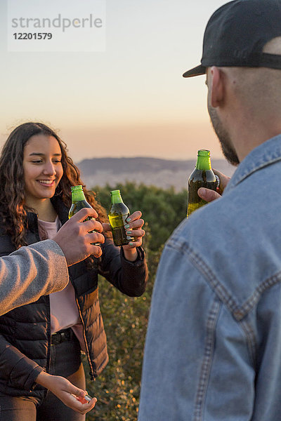 Fröhliche Freunde  die bei Sonnenuntergang im Freien Bierflaschen klirren.
