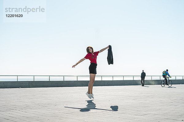 Modische junge Frau beim Springen auf der Uferpromenade