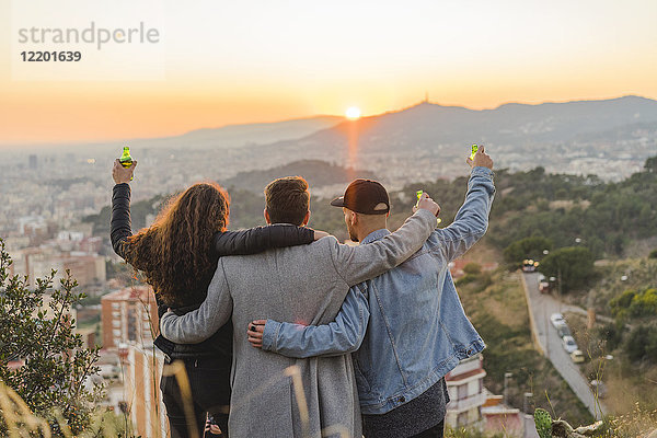 Spanien  Barcelona  drei Freunde mit Bierflaschen auf einem Hügel mit Blick auf die Stadt bei Sonnenuntergang