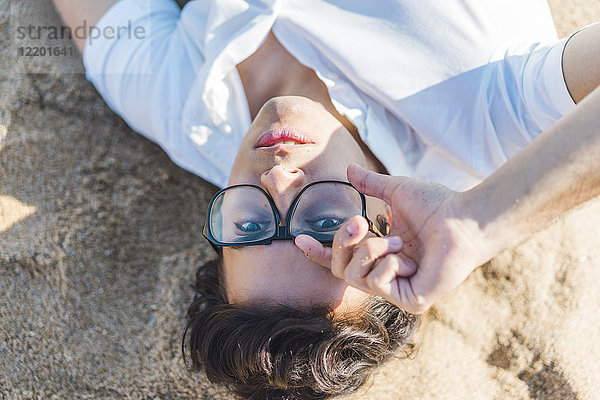 Portrait eines jungen Mannes mit Brille im Sand am Strand liegend